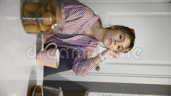 垂直视频年轻美丽的黑发女人喝咖啡吃饼干在家里厨房视频的预览图