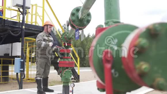 油工在橙色头盔和防护玻璃关闭阀的x质量井口关闭井石油减少视频的预览图