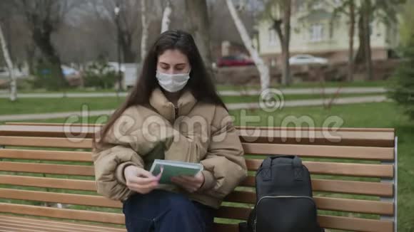 戴防护面具的年轻女子在城市公园的笔记本上写字大流行Covid19冠状病毒保护视频的预览图