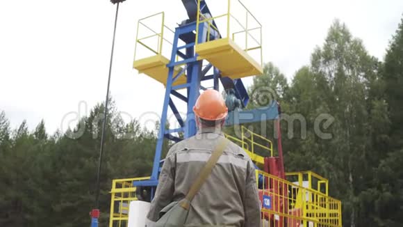 油田技术工人背对着摄像机站在原油泵机组前戴橙色头盔的油工视频的预览图