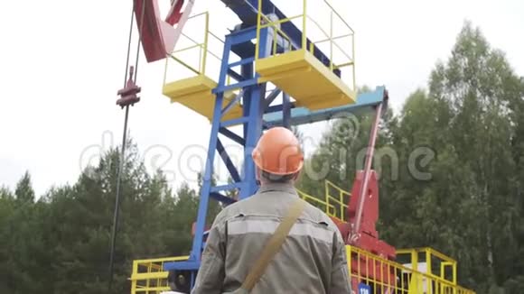 油田技术工人站在原油泵机组前工程师在橙色头盔监督现场原油视频的预览图