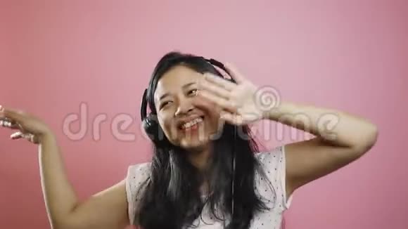 美丽的亚洲女孩跳舞听音乐耳机粉红色背景视频的预览图