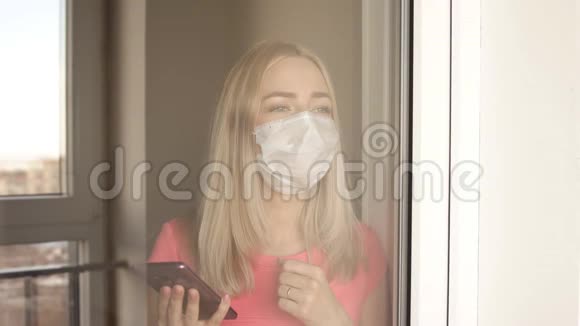 戴着Covid19防护面具的女孩站在窗口很伤心视频的预览图
