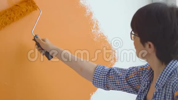 平面改造概念快乐的中年妇女用油漆滚筒画白色的墙橙色的油漆视频的预览图