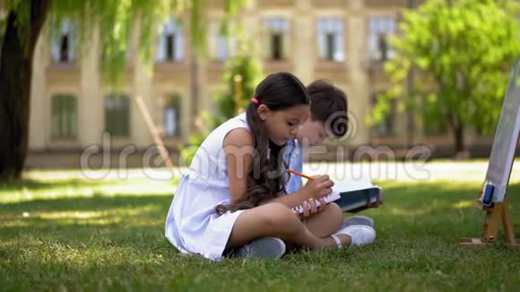 女孩和男孩坐在草地上写着笔记本视频的预览图