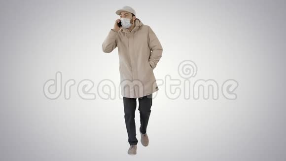 休闲男子穿着户外服装和医用口罩在梯度背景下在电话上行走和交谈视频的预览图