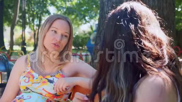 两个快乐的孕妇金发和黑发坐在夏季公园谈笑风生视频的预览图