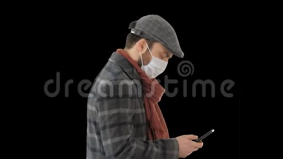 时尚男士戴着医用口罩走路和使用智能手机阿尔法频道视频的预览图