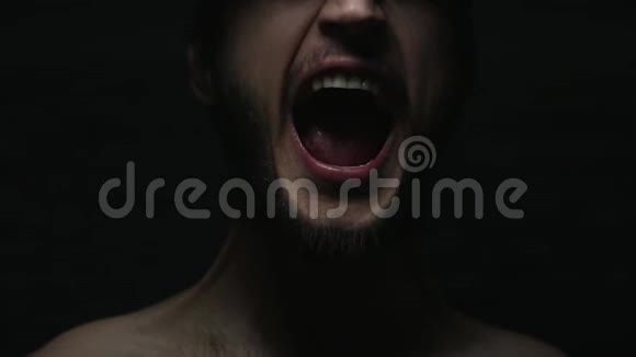 黑色背景下男性嘴巴尖叫的黑暗特写肖像视频的预览图