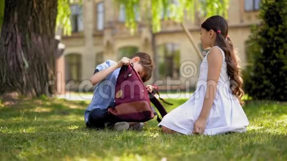 男孩和女孩正坐在学校附近的草坪上休息和聊天视频的预览图
