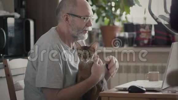 一个拿着宠物在笔记本电脑上工作的老人视频的预览图