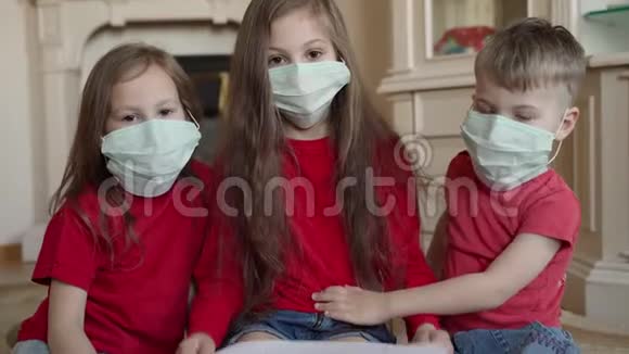 家庭呆在家里的概念三名戴口罩的儿童在家中等候病毒保护并照顾他们视频的预览图