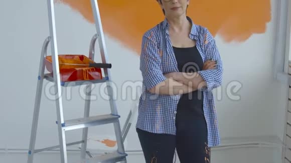 平面改造概念快乐中年妇女用油漆滚筒画白色墙壁橙色油漆视频的预览图
