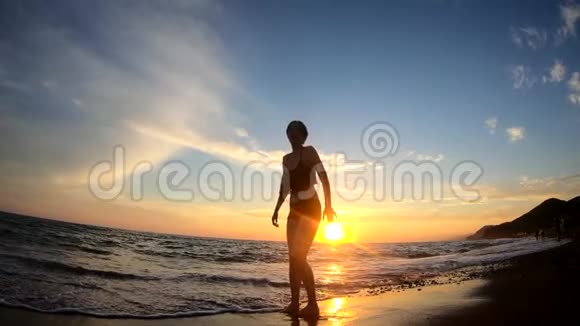 快乐的年轻女子在沙滩上反复跳跃金色的夕阳背景视频的预览图