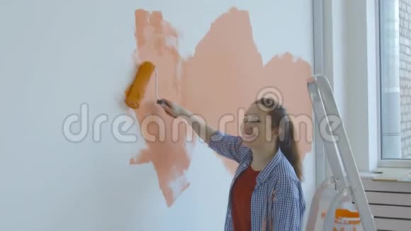 单身生活方式概念年轻快乐的女人用滚筒把墙壁涂成橙色视频的预览图