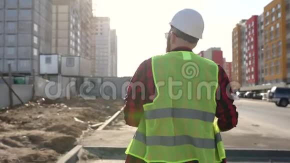 职业工人戴着硬帽子拍摄蓝图走过现代建筑工地视频的预览图