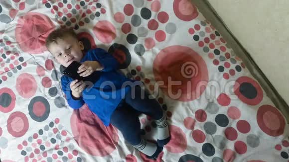 孩子躺在床上看着电子智能手机显示器视频的预览图