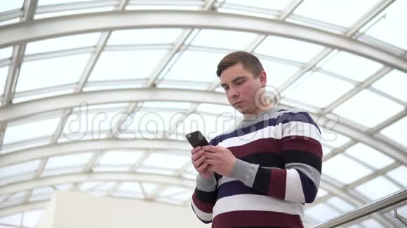 一个年轻人拿着电话站着一个男人用智能手机对着一个玻璃屋顶一个忙碌的人正在发短信视频的预览图