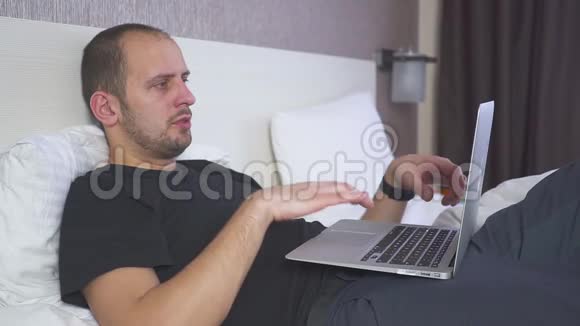 在床上工作的人在笔记本电脑上工作真的想睡觉揉他的眼睛视频的预览图
