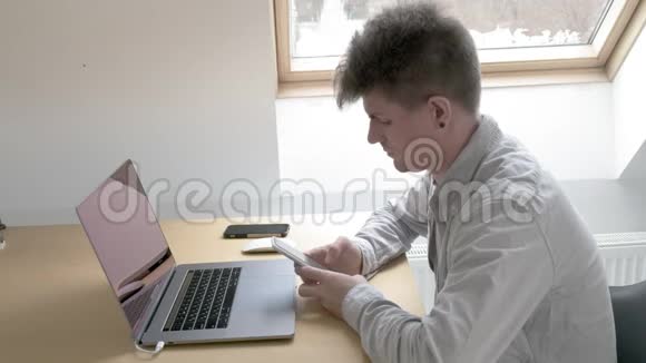 男人坐在电脑桌前盯着智能手机在家庭办公室工作视频的预览图