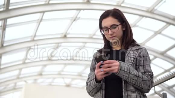 一个年轻的女人拿着电话站着一个女孩用智能手机对着一个玻璃屋顶一个忙碌的人正在发短信视频的预览图