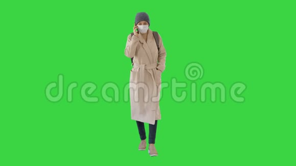 年轻女子戴着防护面具在绿色屏幕上用手机走路和说话Chroma键视频的预览图