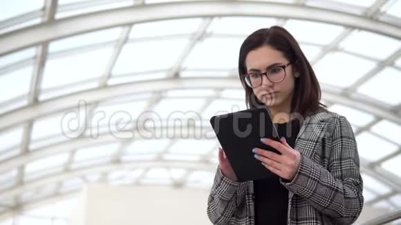 一个年轻的女人拿着一块药片站着一个女孩用平板电脑对着一个玻璃屋顶一个忙碌的人正在发短信视频的预览图