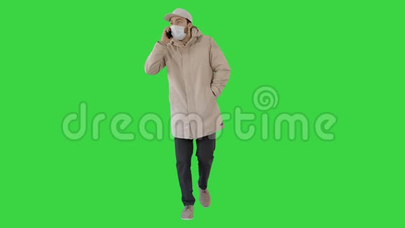 穿着户外衣服和医用面具的休闲男子在绿色屏幕上行走和在电话上交谈Chroma键视频的预览图