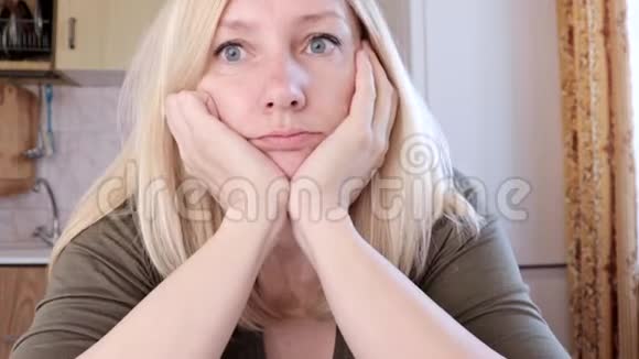 一个悲伤而无聊的年轻金发女人坐在厨房的肖像悲伤和抑郁的概念视频的预览图