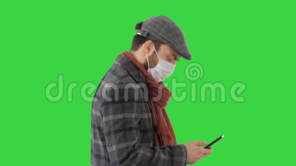 时尚男子在医疗面具行走和使用智能手机的绿色屏幕铬键视频的预览图