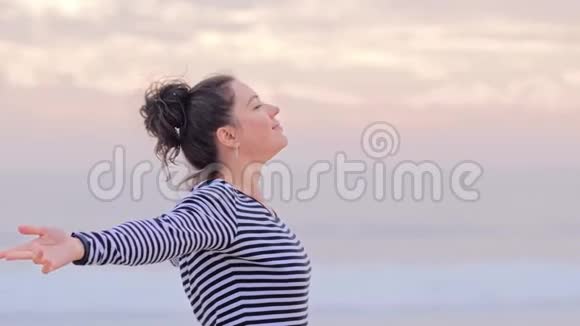 快乐的女人在海滩上挽着条纹衬衫享受日落视频的预览图