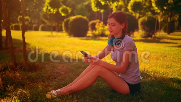 欢快的女性听音乐坐在绿草上视频的预览图