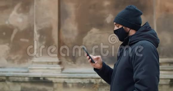 人行走和使用智能手机在社交网络中交流的侧面视图穿着黑棉衣服的男人视频的预览图