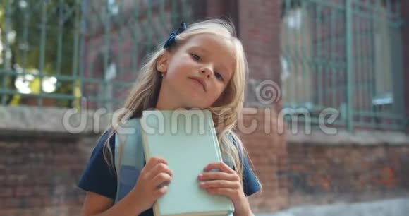 可爱的小女生拿着书看着镜头的肖像一头金色长发的可爱孩子视频的预览图