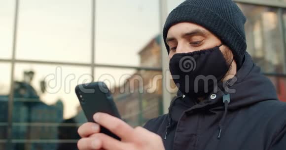 当站在街上时请关闭男子打字信息的视图穿着黑色棉防护面罩的男人用视频的预览图