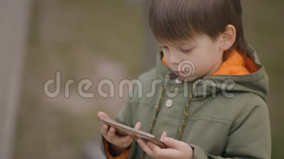 两个年轻可爱的双胞胎男孩穿绿色春季夹克用手机看动画片烟瘾概念视频的预览图