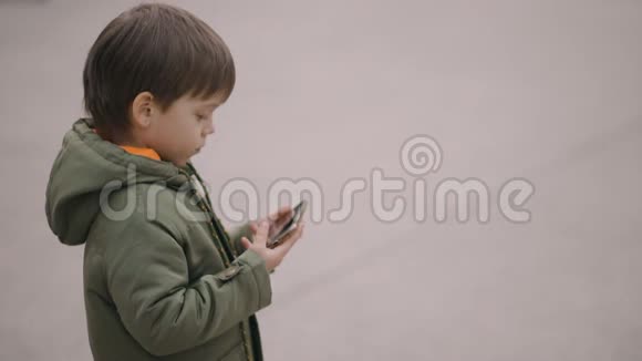 可爱的男孩穿绿色春夹克用手机烟瘾概念慢动作复制空间镜头视频的预览图