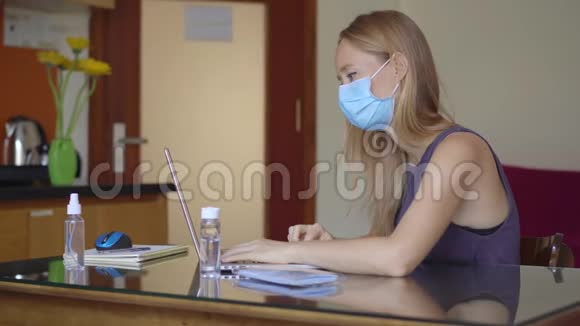 一位戴着医用面罩的年轻女子在冠状病毒自我隔离期间在家工作远程工作概念视频的预览图