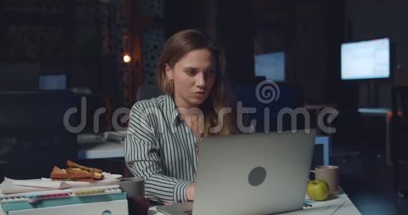 睡意朦胧的年轻女子深夜在办公室工作的肖像疲惫的女上班族用她的笔记本电脑打字视频的预览图