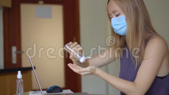 一位戴着医用面罩的年轻女子在冠状病毒自我隔离期间在家工作她用洗手液视频的预览图