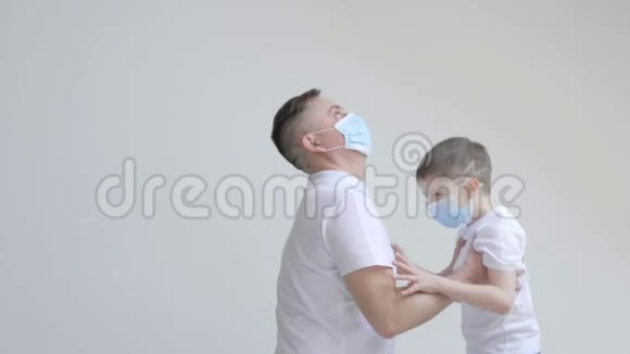 年轻的父亲和他的儿子在工作室里玩得很开心在白色背景的隔离期间戴上口罩以保护视频的预览图