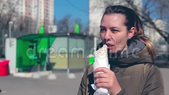 街上的一个年轻女孩吃一个甜甜圈女孩在路边吃快餐晴天视频的预览图
