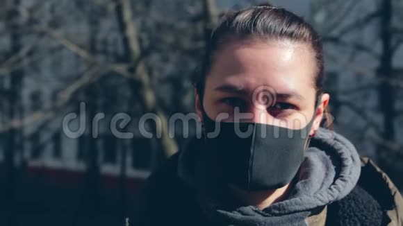 穿着黑色防护面具的女孩看着相机在街道上在多层建筑的背景下视频的预览图