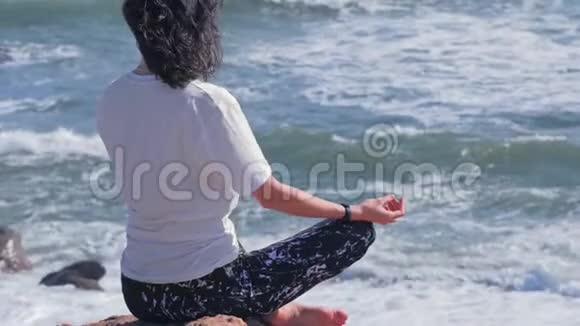 女人在海边的岩石上坐在莲花的位置上视频的预览图