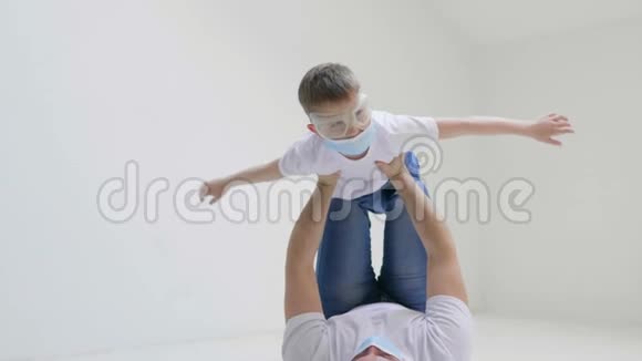 年轻的父亲和他的儿子在工作室里玩得很开心在白色背景的隔离期间戴上口罩以保护视频的预览图