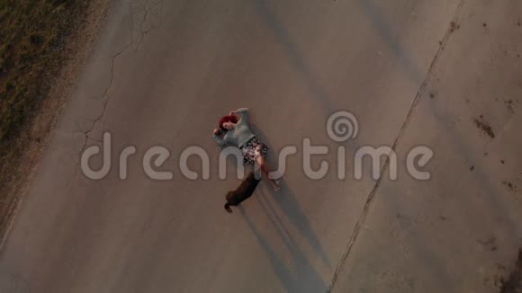 空中景色年轻的红发女子躺在柏油路上在日落时分和狗狗玩耍视频的预览图