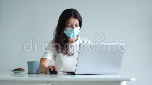 这女孩在隔离期间在家工作电晕病毒大流行一个戴手术面罩的女孩在笔记本电脑上工作喝咖啡视频的预览图