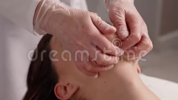 美容水疗中心健康按摩治疗的年轻女性按摩治疗师正在做手工颊部按摩视频的预览图