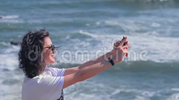 快乐的女人用智能手机相机拍摄海洋视频的预览图