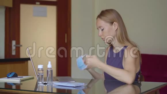 一名年轻女子戴上医用面罩在冠状病毒自我隔离期间在家工作视频的预览图